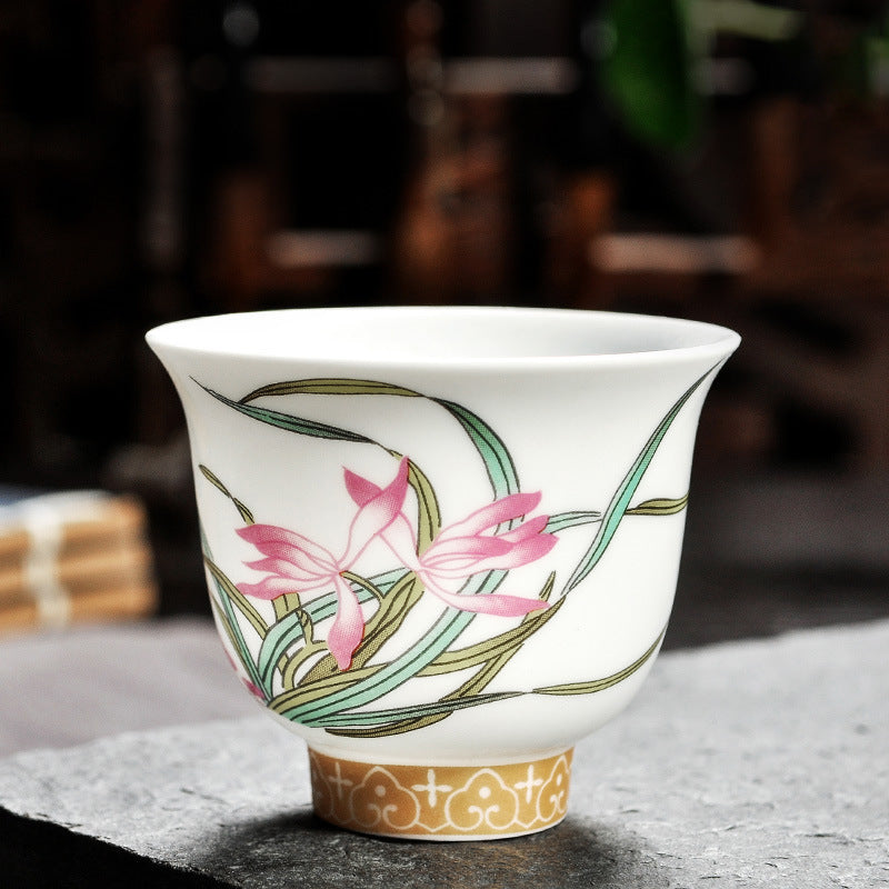 Dehua porcelain tea cup with pink flowers, long green leaves and a gold-colored patterned base