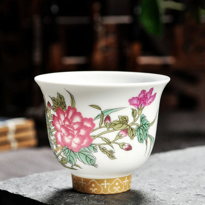 Dehua porcelain tea cup with red and pink flowers, green foliage and a gold-colored patterned base