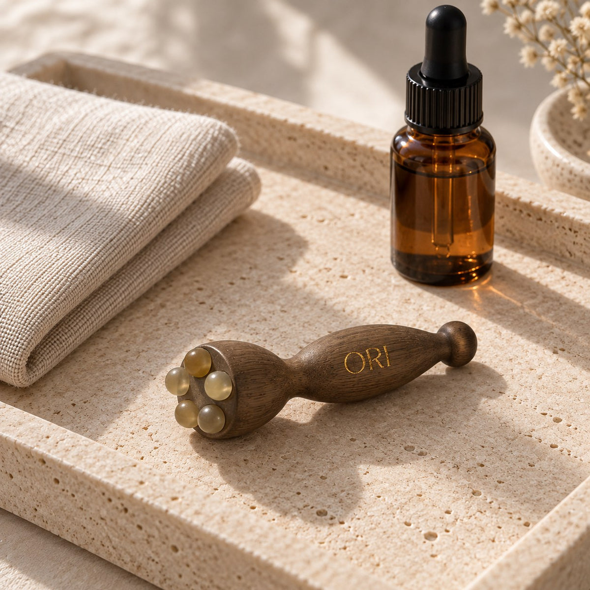 Green sandalwood eye massage tool: On stone beside folded towels and a dropper bottle