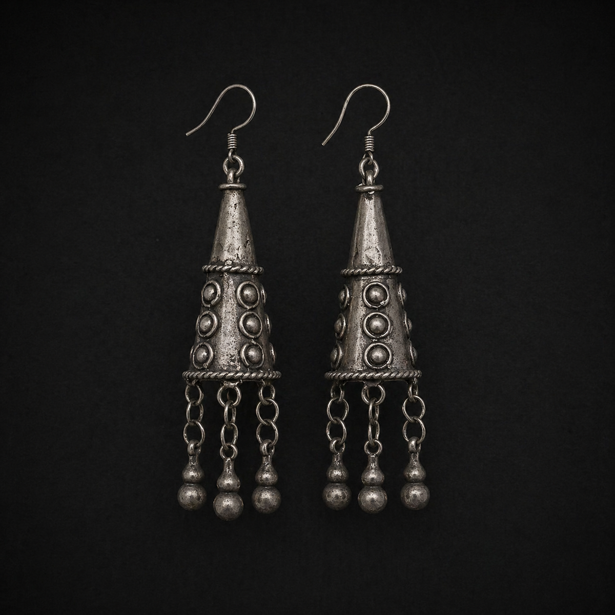 Miao silver tassel drop earrings: Pair on a dark background showing patterned cones and chains