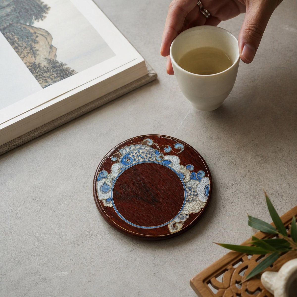 Round red sandalwood cloisonne coaster: Blue floral design beside a book and white cup
