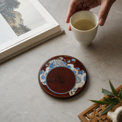 Round red sandalwood cloisonne coaster: Blue floral design beside a book and white cup