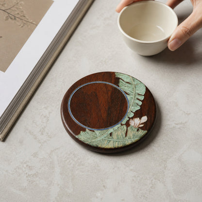 Round red sandalwood cloisonne coaster: Green botanical design beside a book and white cup