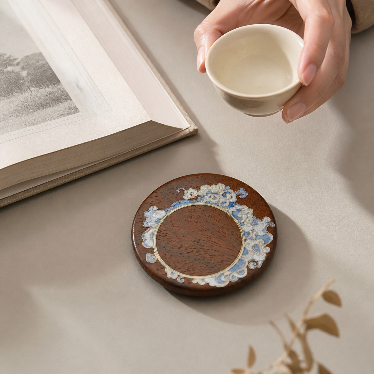 Round red sandalwood cloisonne coaster: Pale blue floral design beside a hand holding a white cup