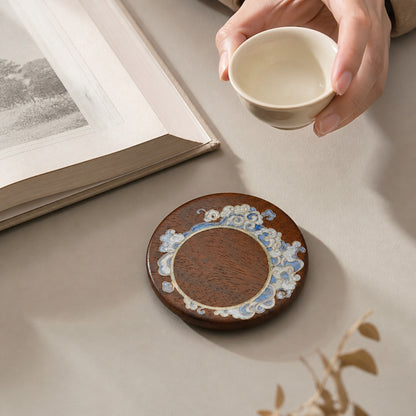 Round red sandalwood cloisonne coaster: Pale blue floral design beside a hand holding a white cup