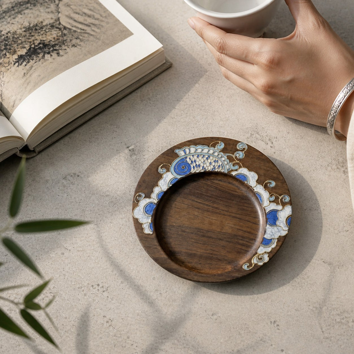 Round walnut cloisonne coaster: Blue floral design on a pale table beside a book