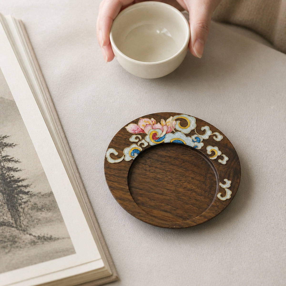 Round walnut cloisonne coaster: Pink floral design beside a hand holding a white cup