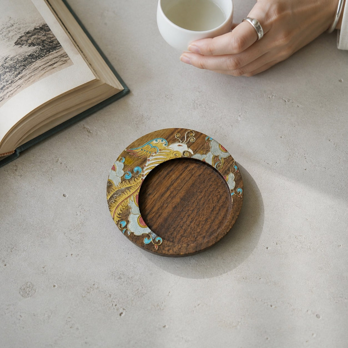 Round walnut cloisonne coaster: Yellow floral design beside a book and white cup