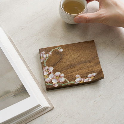 Square walnut cloisonne coaster: Pale blossom design beside a hand holding a cup