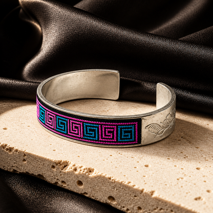 Xixiu embroidered silver cuff: Pink and blue cuff on pale stone beside dark fabric
